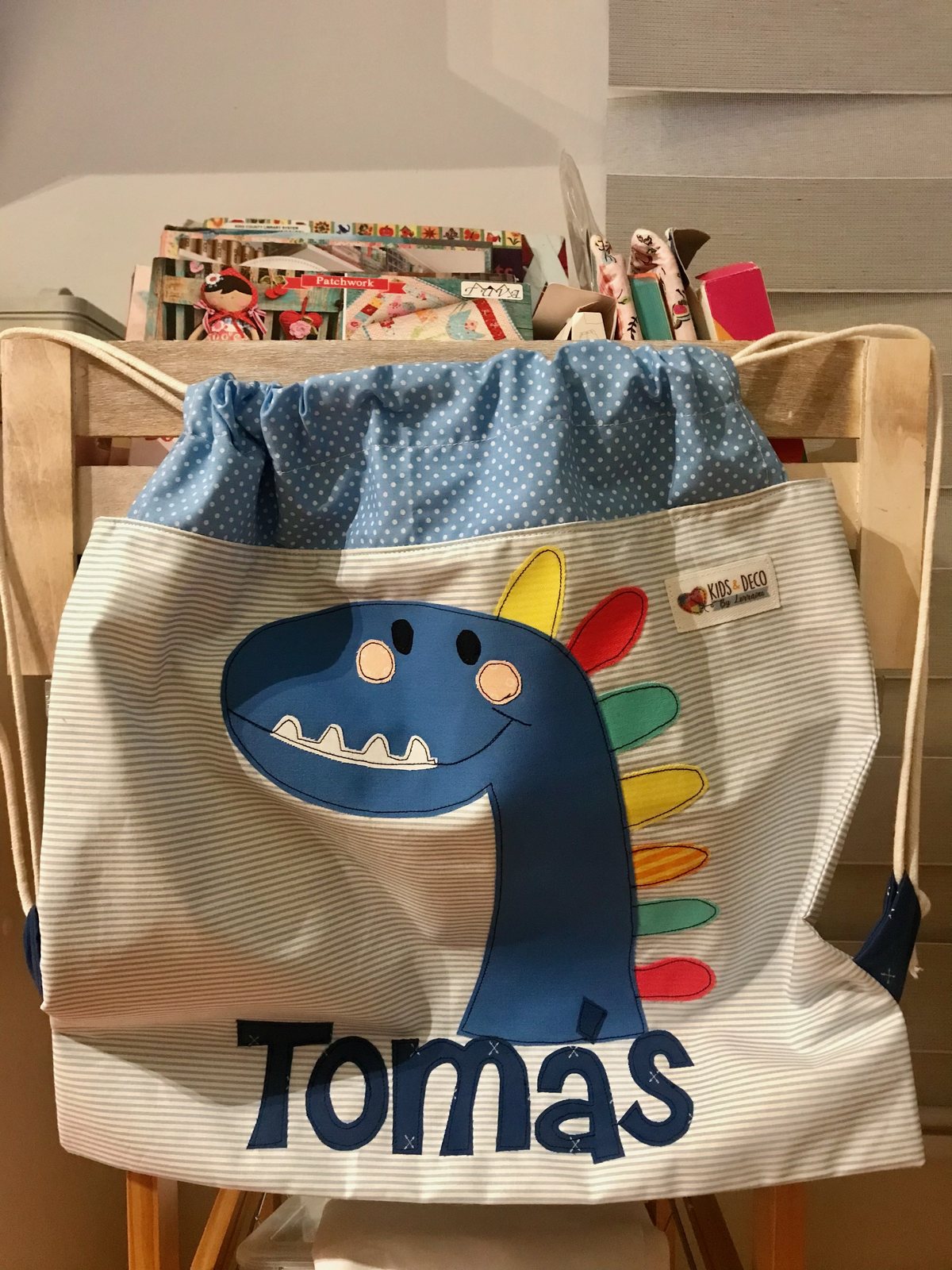 Morral crema con un dinosaurio azul y el nombre Tomás