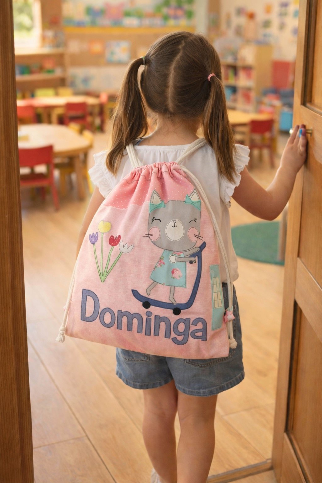 Niña de espaldas entrando a la sala del jardín con un morral rosado que dice Dominga
