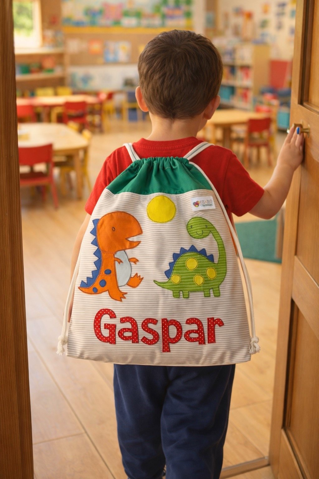 Niño de espaldas con un morral de dinosaurios que dice Gaspar